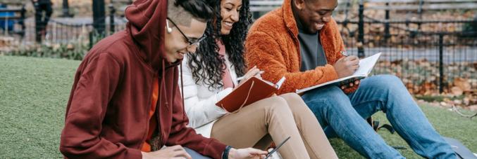 young people sitting on a lawn with books and laptops